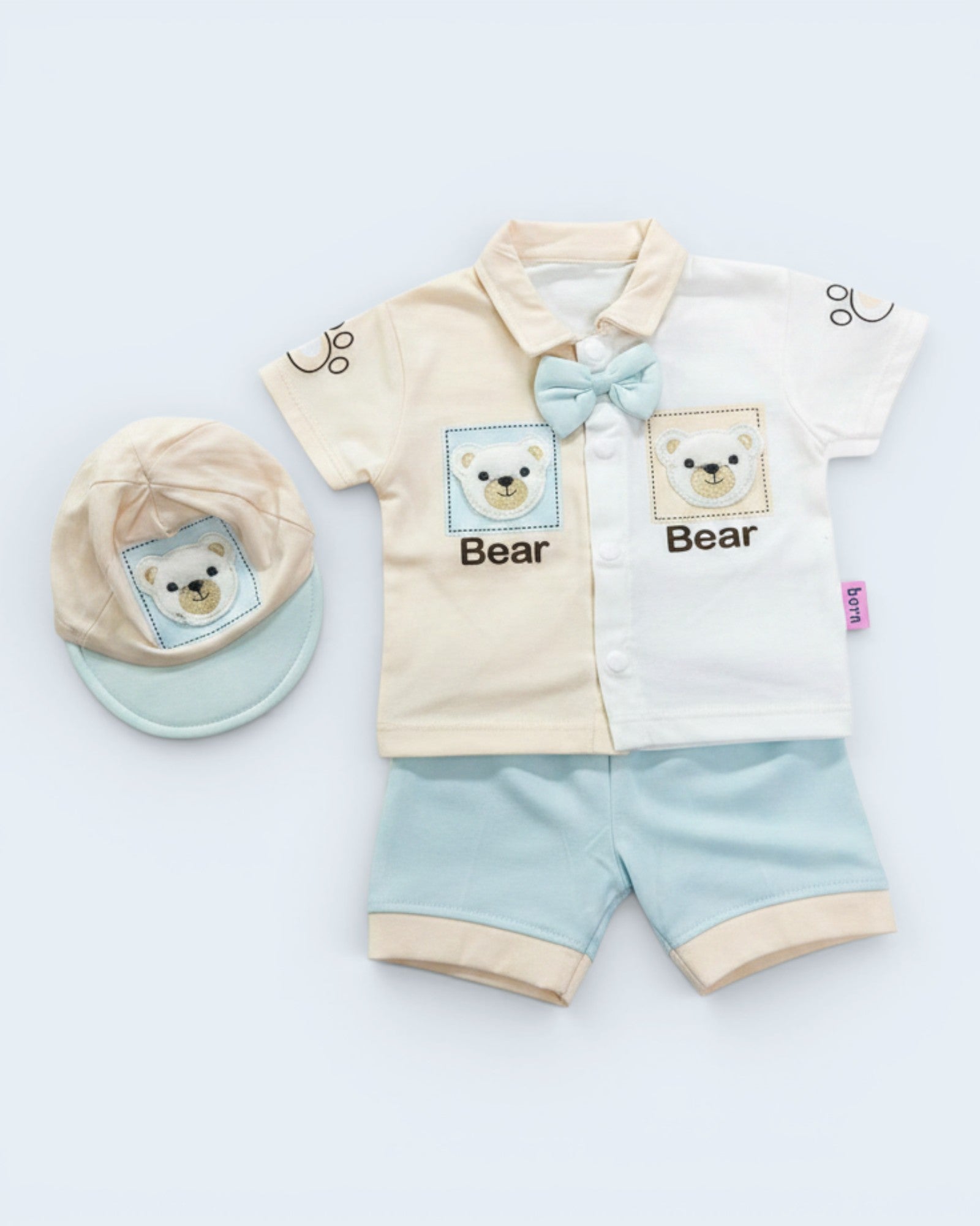 Little Roots baby boy 3-piece outfit set with bear design, bow tie, shorts, and cap. Cream and white color block shirt with blue accents.