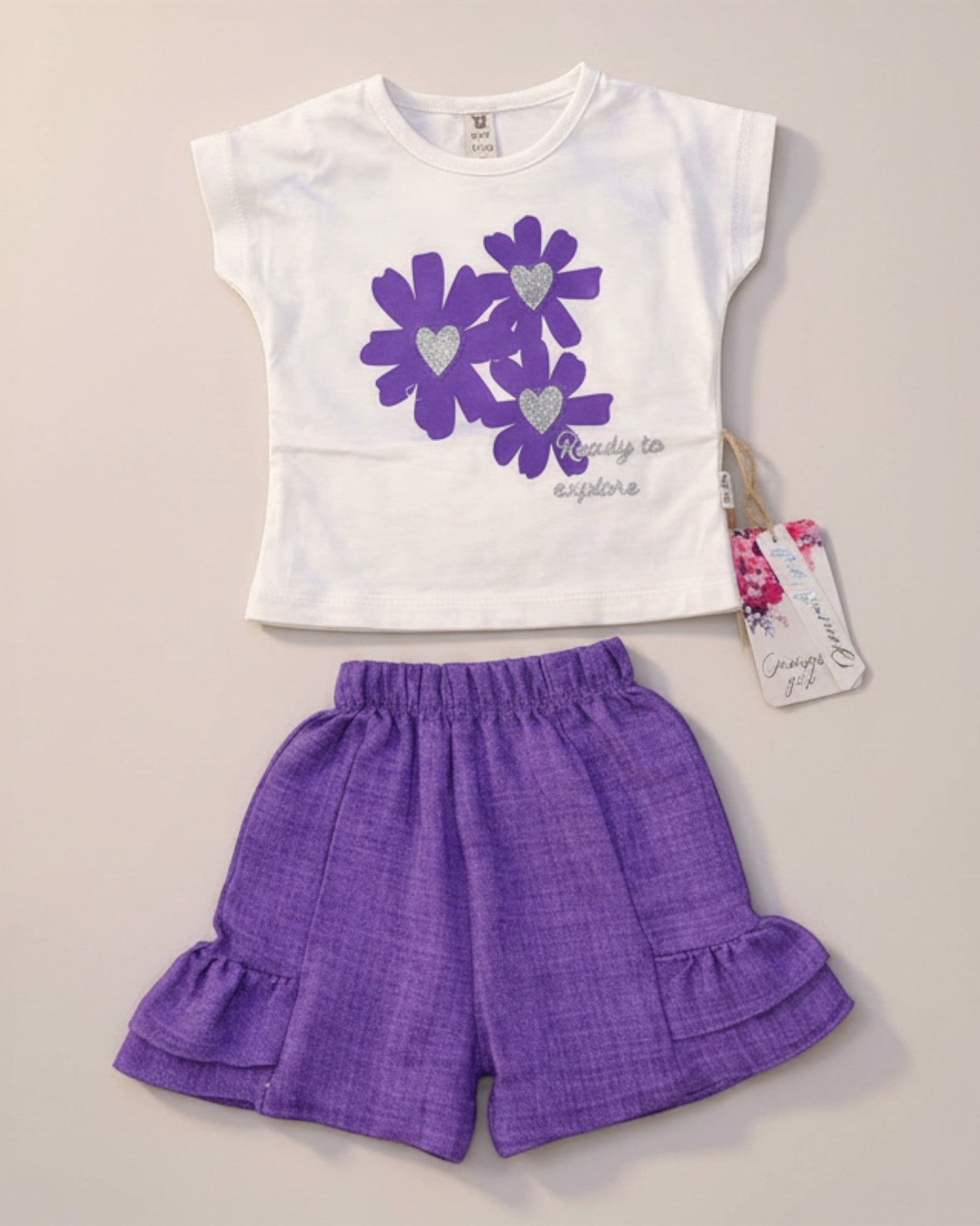 Little Roots Pakistan white t-shirt with purple floral print and glitter hearts, paired with purple ruffle shorts. "Ready to explore" text.