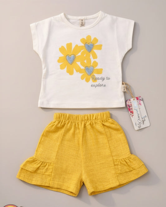 Little Roots Pakistan cream t-shirt with yellow floral print and glitter hearts, paired with yellow ruffle shorts. "Ready to explore" text.
