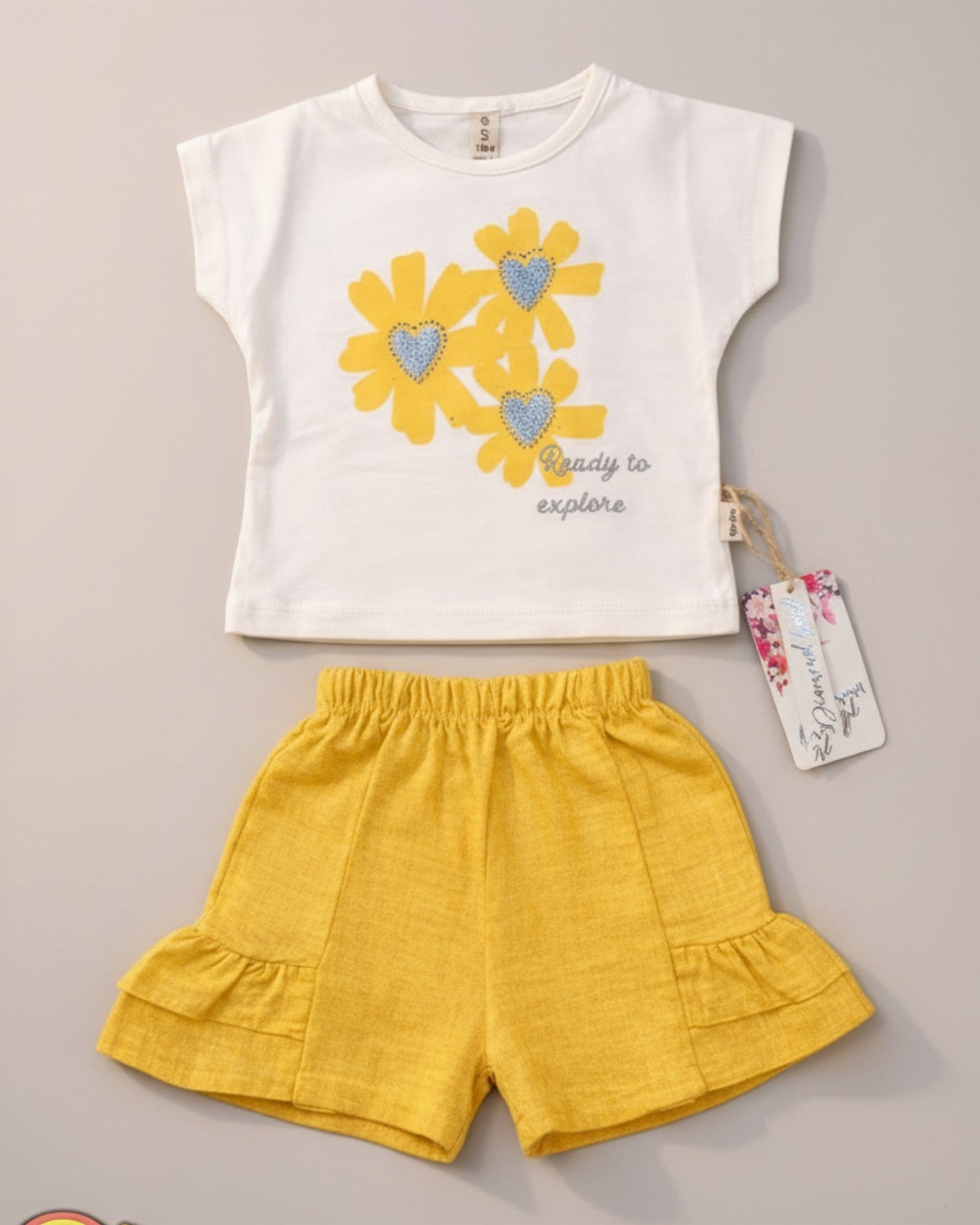 Little Roots Pakistan cream t-shirt with yellow floral print and glitter hearts, paired with yellow ruffle shorts. "Ready to explore" text.