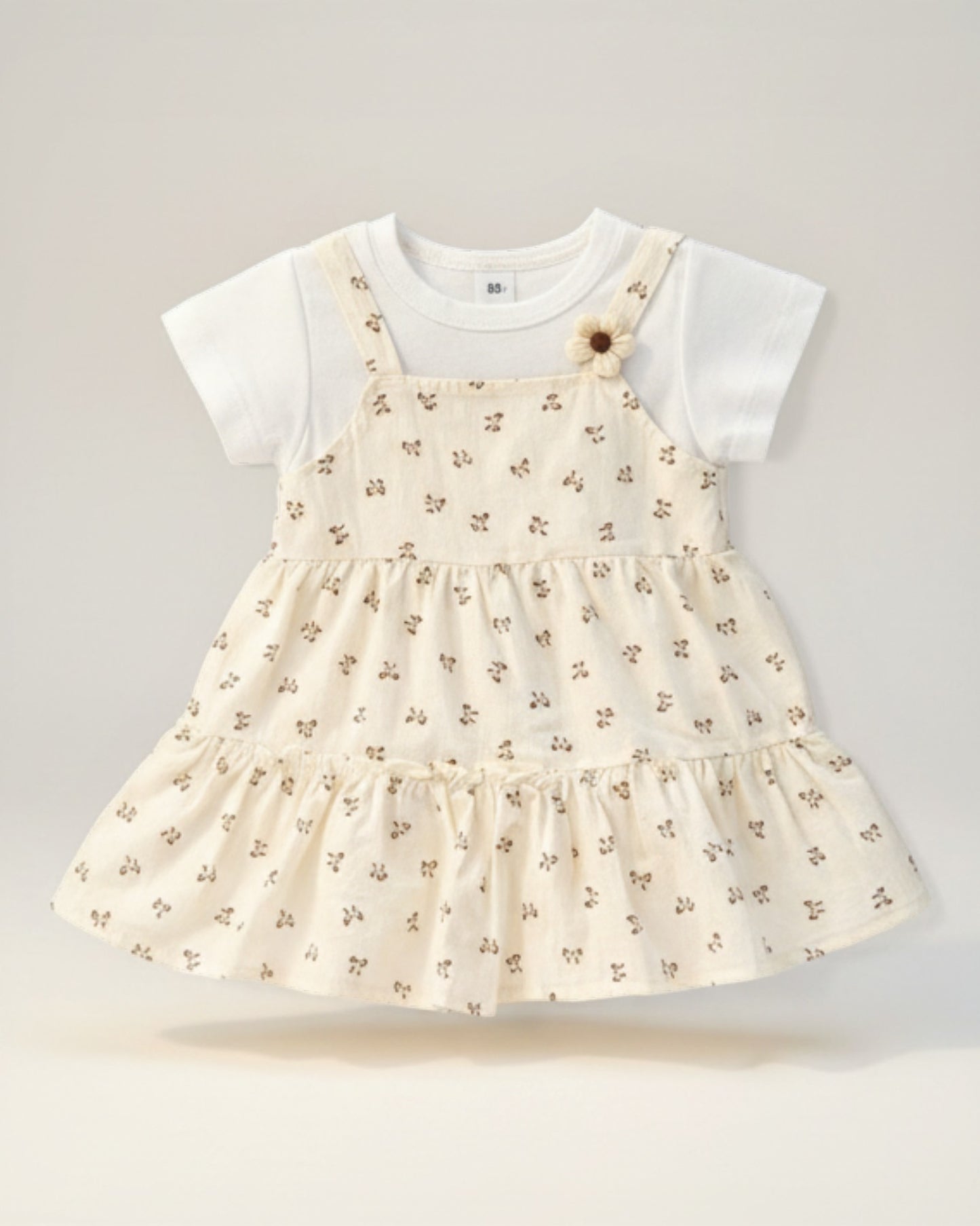 Little Roots cream floral print baby girl dress with layered hem and flower strap detail. Soft cotton fabric.