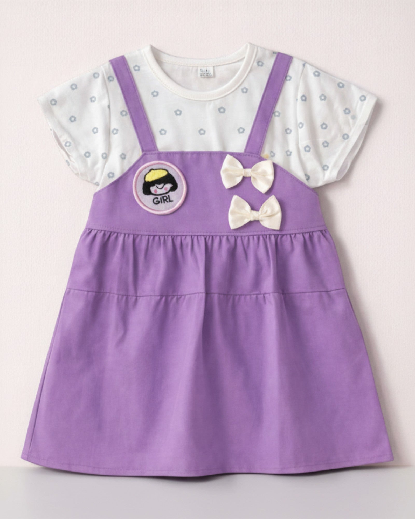 Little Roots baby girl purple pinafore dress with white floral print top, "Girl" patch, and double bow accents.